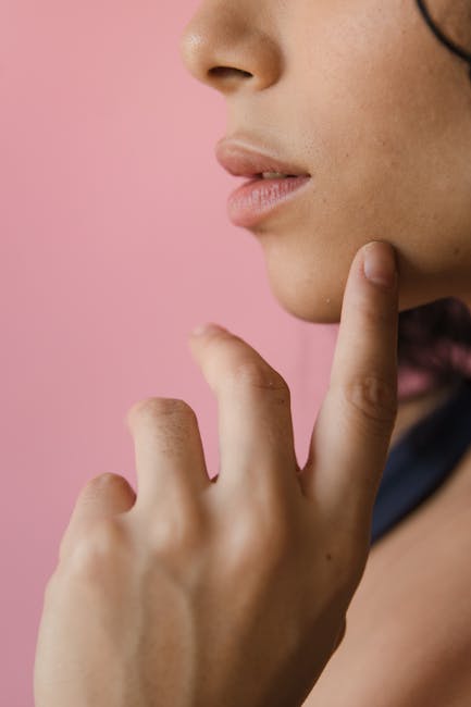 Close-up of a woman's chin and fingers against a pink background, suggesting contemplation.